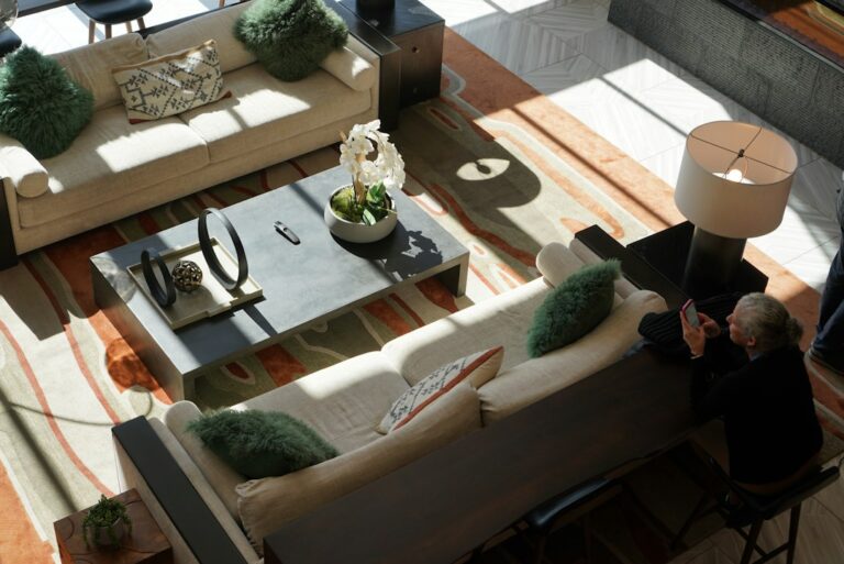 A couple measures a sofa footprint in a bright living room beside fabric samples and a tape measure.
